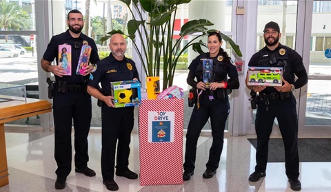 Police officers holding toys next to donation box.